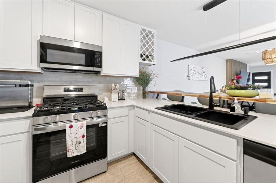 Modern kitchen featuring white shaker cabinetry, stainless steel appliances, a double basin sink with matte black faucet, light stone countertops, and a full-height tile backsplash