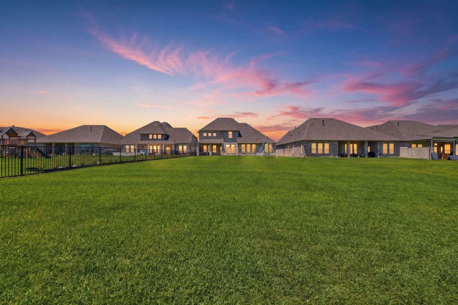 This photo showcases a row of modern homes with spacious backyards, set against a picturesque sunset sky. The wide expanse of green lawn offers ample space for outdoor activities.