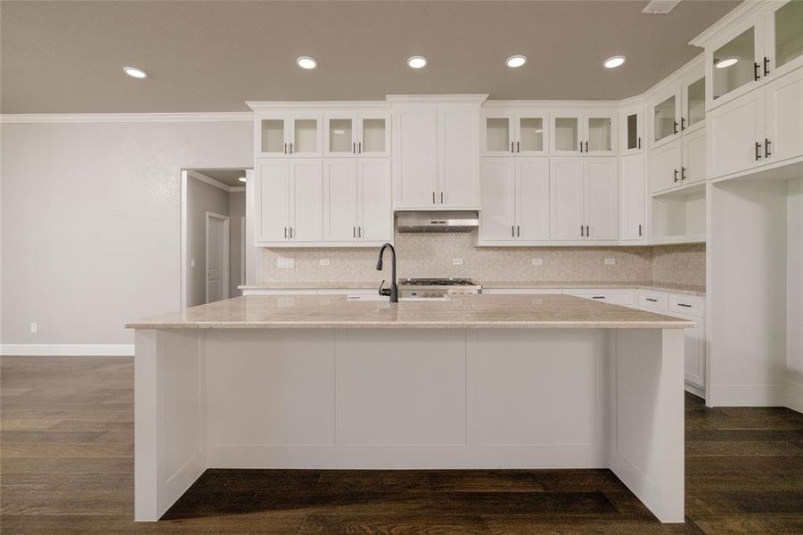 Kitchen with under cabinet range hood, ornamental molding, decorative backsplash, and an island with sink Kitchen with under cabinet range hood, ornamental molding, decorative backsplash, and an island with sink