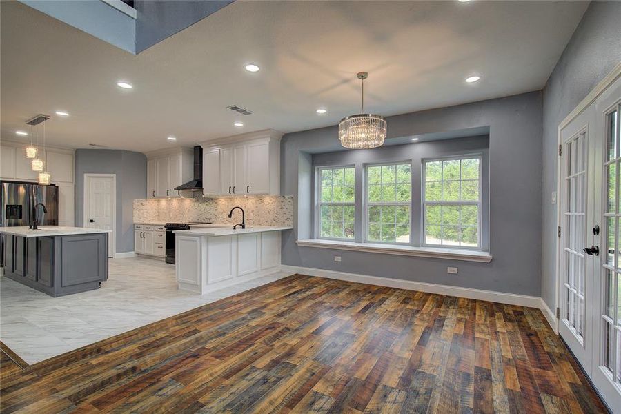 Dining area with light hardwood / wood-style floors, pendant lighting, backsplash, and wall chimney exhaust hood