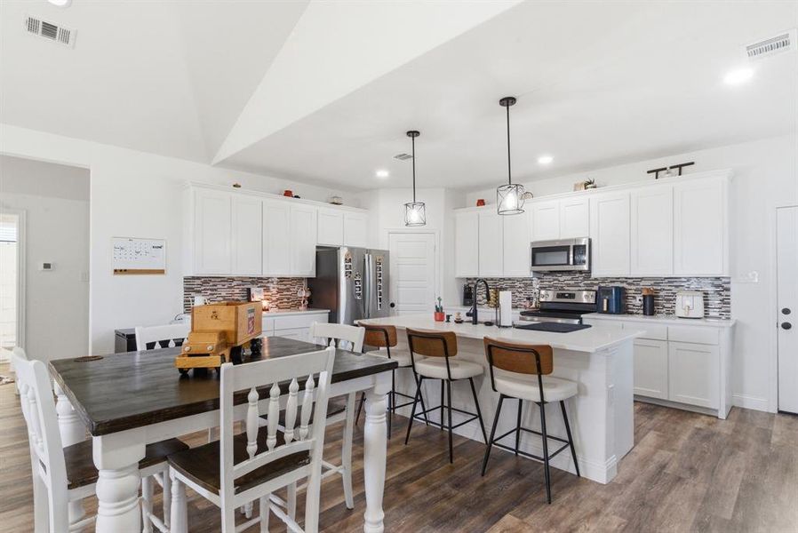 Kitchen featuring a breakfast bar, white cabinetry, an island with sink, and dark wood-type flooring Kitchen featuring a breakfast bar, white cabinetry, an island with sink, and dark wood-type flooring