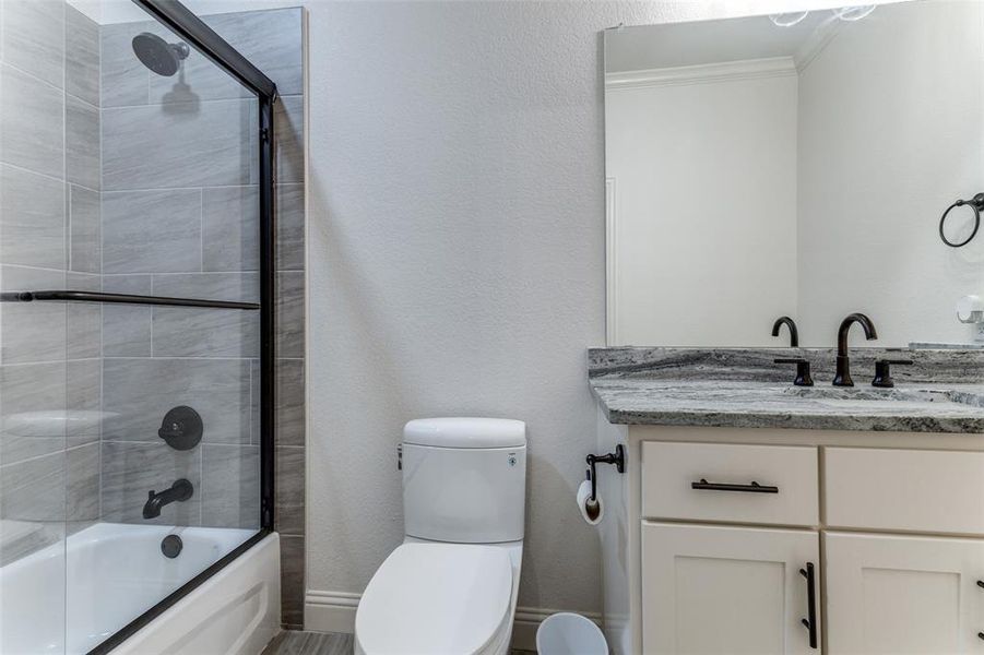 Bathroom featuring vanity, shower / bath combination with glass door, and ornamental molding
