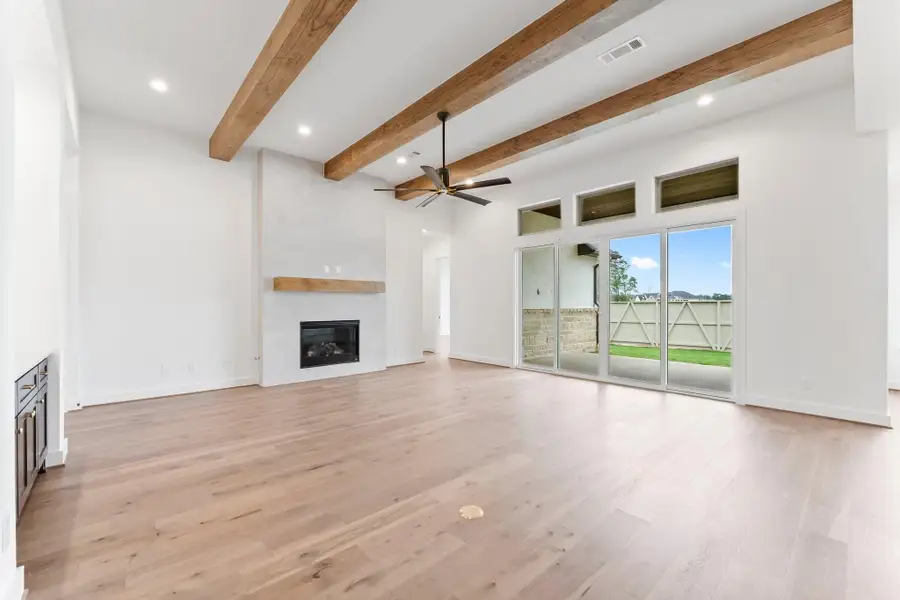 Great Room Adorned with Wood Beams, Gas-Log Fireplace, and Sliding Doors that Lead to the Covered Rear Patio.