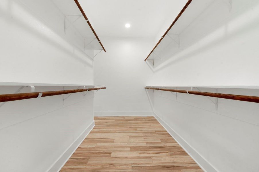 Spacious walk-in closet with wooden flooring, ample hanging space, and bright lighting. Ideal for organized storage. Spacious walk-in closet with wooden flooring, ample hanging space, and bright lighting. Ideal for organized storage.