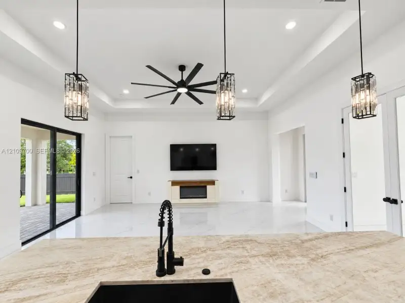 Tray ceiling with recessed lighting and a multi-blade ceiling fan, expansive stone-finish flooring, and natural stone kitchen island countertop featuring a matte black industrial faucet and undermount sink