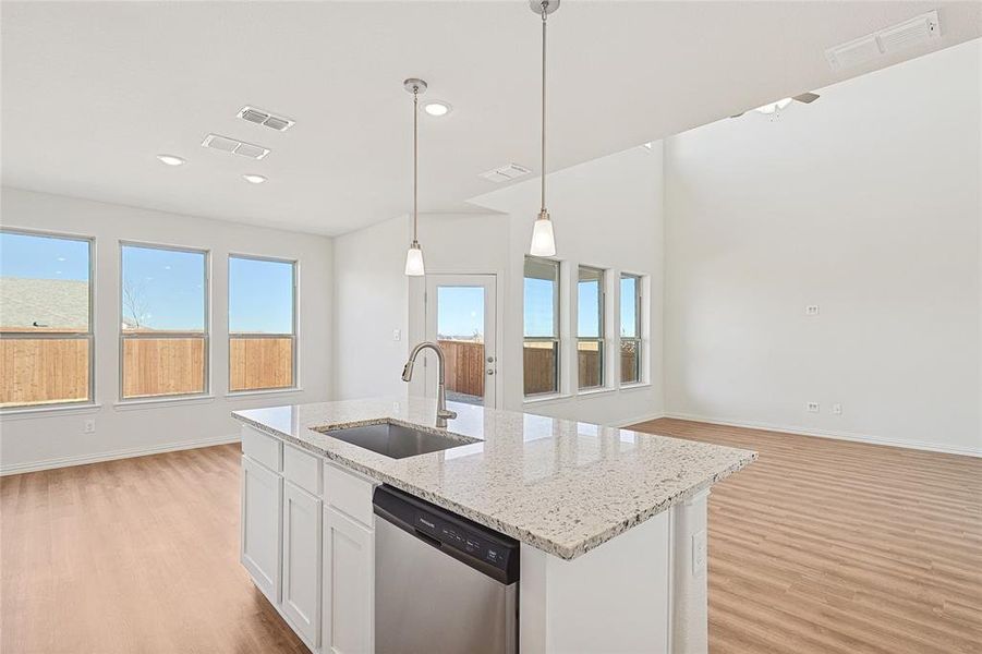 Kitchen with open floor plan, light wood-style flooring, white cabinets, dishwasher, and light stone countertops