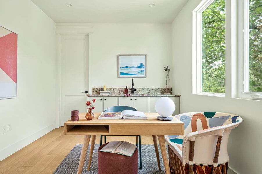 Natural light floods this versatile space, featuring a functional wet bar and rich hardwood flooring.