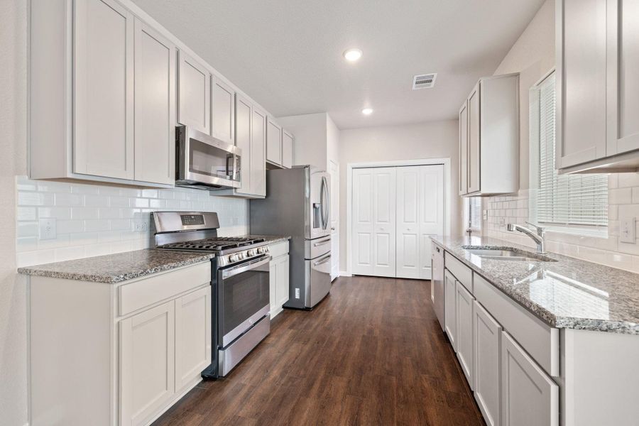 Kitchen featuring appliances with stainless steel finishes, backsplash, light stone counters, dark wood-style flooring, and recessed lighting