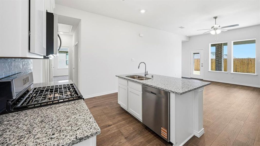 Kitchen with light stone counters, white cabinets, appliances with stainless steel finishes, dark wood-style floors, and a center island with sink