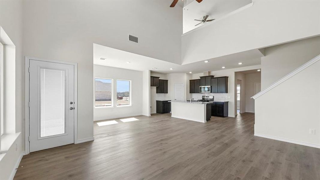 Unfurnished living room featuring ceiling fan, dark wood-style floors, and a towering ceiling