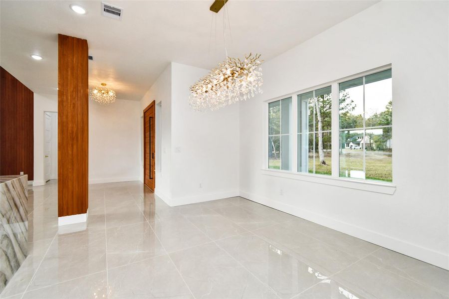The bright and airy dining area is framed by large picture windows, offering serene views of the surrounding landscape. The minimalist white walls and polished flooring provide a clean canvas for any decor style, anchored by a luxurious nature-inspired light fixture.