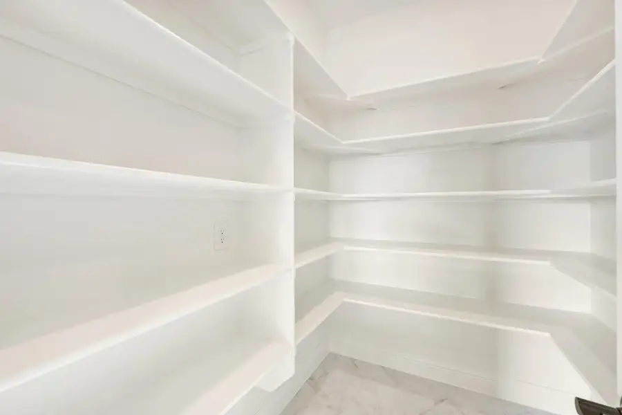 Walk-in pantry with white built-in shelving on three walls and marble tile flooring