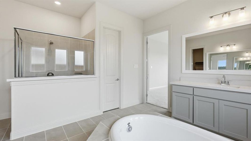 Contemporary bathroom featuring a freestanding tub, a walk-in shower with glass enclosure and tiled walls, a vanity with a light gray cabinet and a rectangular mirror, and light-toned tile flooring