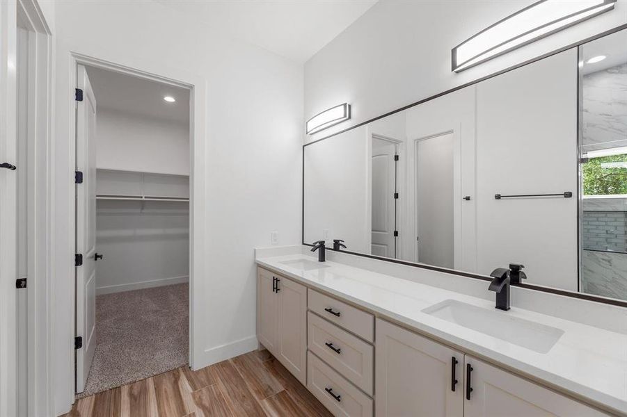 Bathroom featuring a sink, a walk in closet, wood finished floors, and double vanity