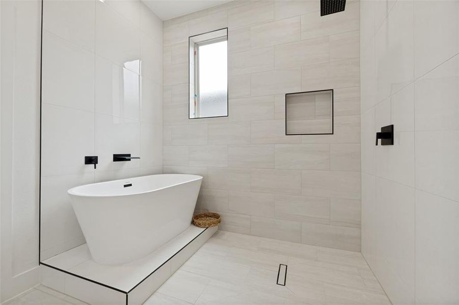 Freestanding soaking tub on a tiled platform, complemented by matte black wall-mounted fixtures