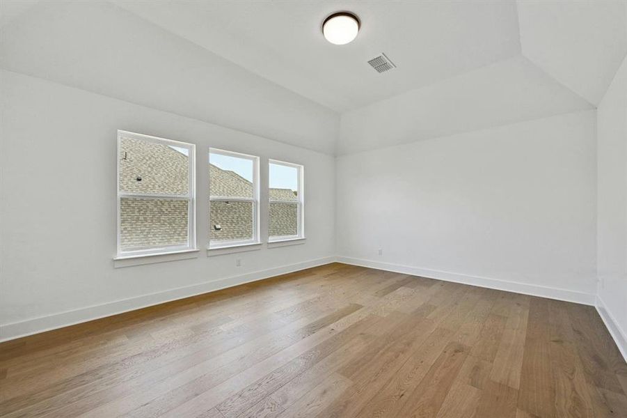 Unfurnished room with light wood-type flooring and vaulted ceiling Unfurnished room with light wood-type flooring and vaulted ceiling