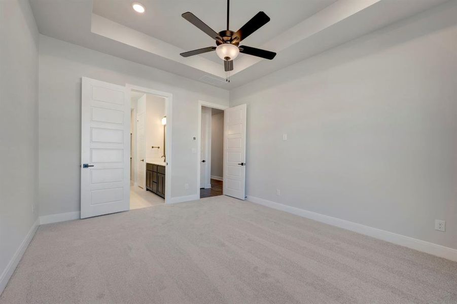 Unfurnished bedroom with light colored carpet, a ceiling fan, connected bathroom, and a tray ceiling