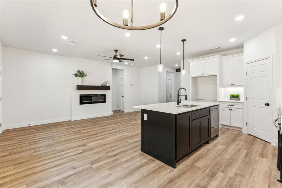 Kitchen featuring open floor plan, a center island with sink, white cabinets, recessed lighting, and decorative light fixtures