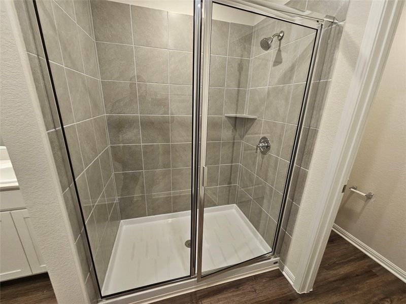 Bathroom featuring dark wood-type flooring, a stall shower, vanity, and a textured wall Bathroom featuring dark wood-type flooring, a stall shower, vanity, and a textured wall
