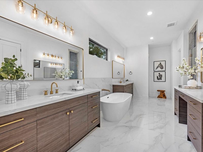 The spa-inspired en-suite showcases dual vanities with framed mirrors, designer lighting, and a freestanding soaking tub. A third “get-ready” vanity with knee space adds convenience, while the oversized shower boasts dual shower heads for a true retreat experience.