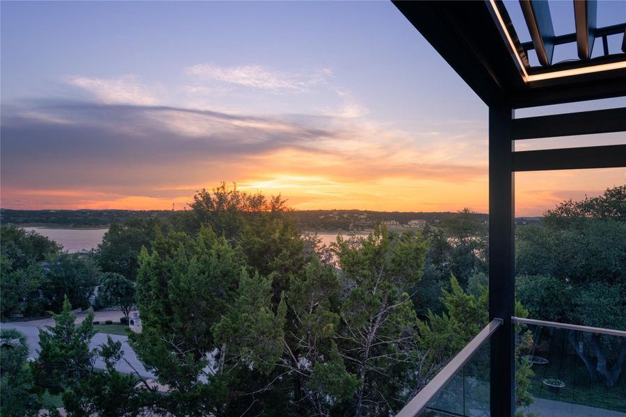 Golden hour illuminates a vast lake panorama, framed by lush tree lines and a modern balcony.