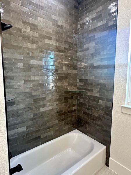 Bathroom with a textured wall and bathing tub / shower combination
