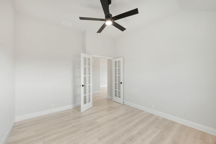 Empty room with light wood floors, black ceiling fan, and white French doors