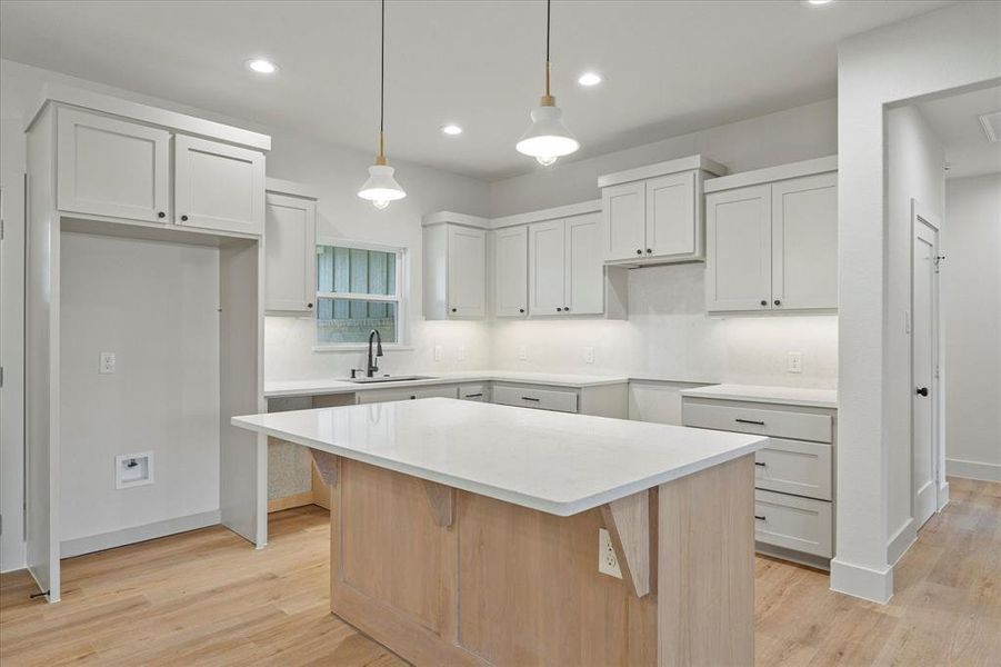 Kitchen with decorative light fixtures, a center island, sink, and light hardwood / wood-style flooring