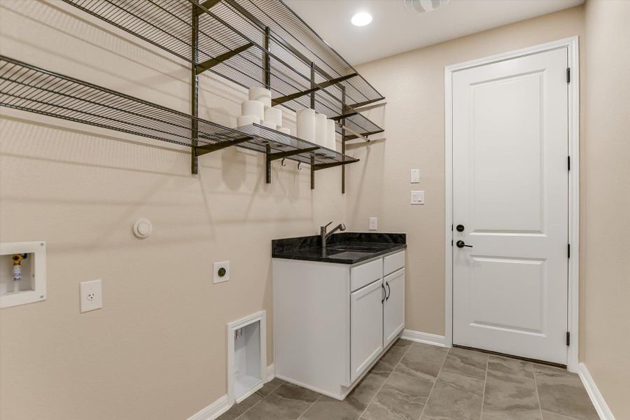 The spacious hall laundry room features ELFA® shelving, a sink with granite counter top, and electric dryer and washing machine hook ups.