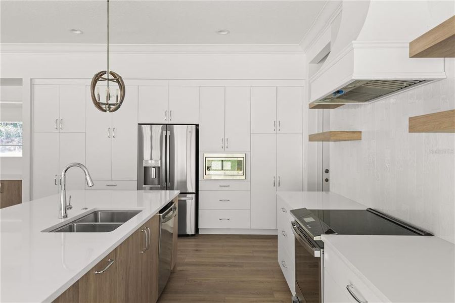 Kitchen detail highlighting the white cabinetry, stainless steel appliances, a center island with a light wood finish and white countertop, pendant lighting, and a modern range hood.