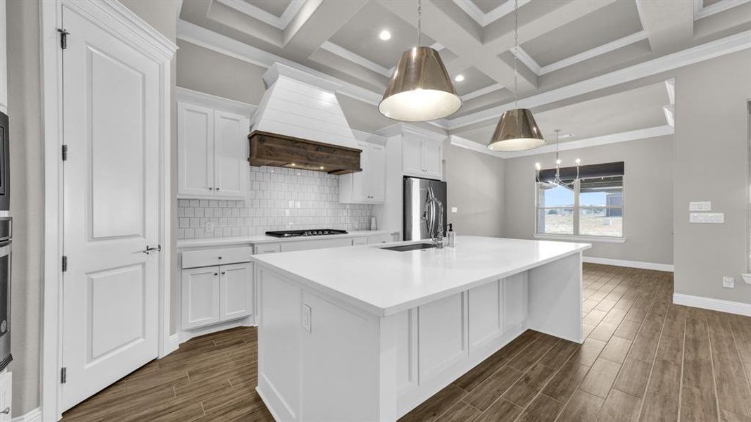 Kitchen featuring an island with sink, backsplash, coffered ceiling, and premium range hood