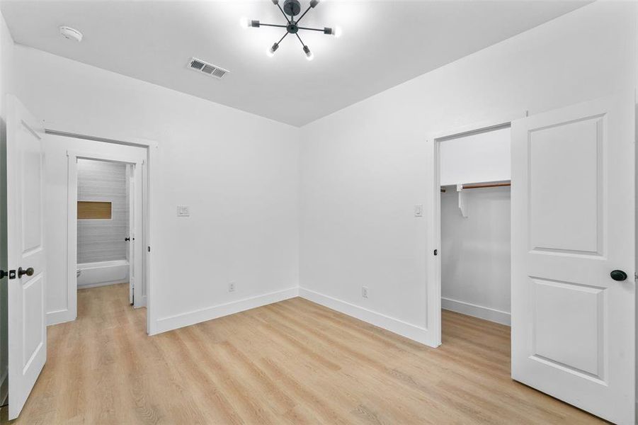Room featuring wood-finish flooring, white walls, and a modern ceiling light fixture Room featuring wood-finish flooring, white walls, and a modern ceiling light fixture