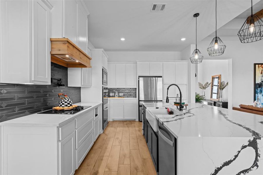 Kitchen featuring appliances with stainless steel finishes, light wood-type flooring, decorative light fixtures, white cabinets, and an island with sink