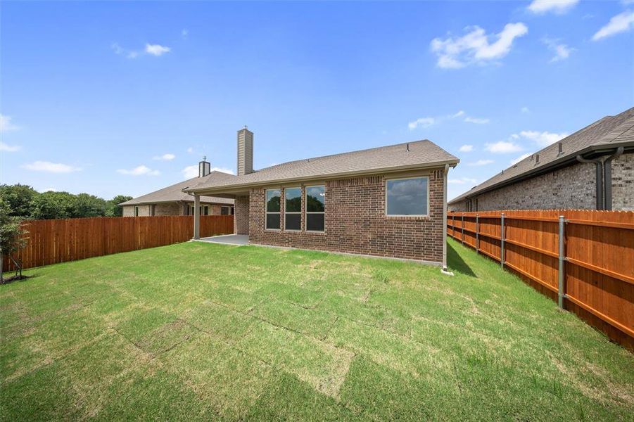 Rear view of property with a chimney, a fenced backyard, brick siding, roof with shingles, and a patio