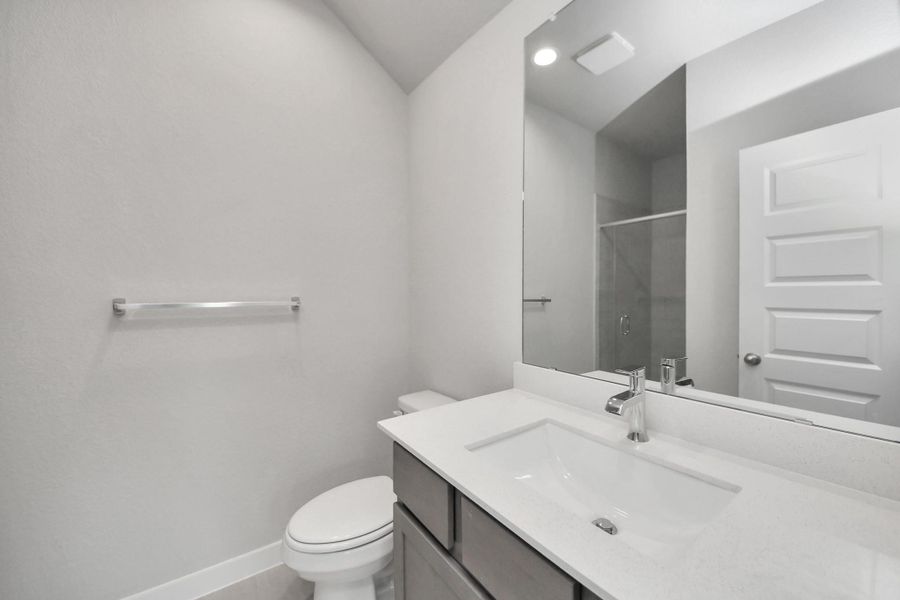 Secondary bath features tile flooring, a walk-in shower with tile surround, light stained wood cabinets, beautiful light countertop. Sample photo of completed home with similar floor plan. Actual colors and selections may vary.