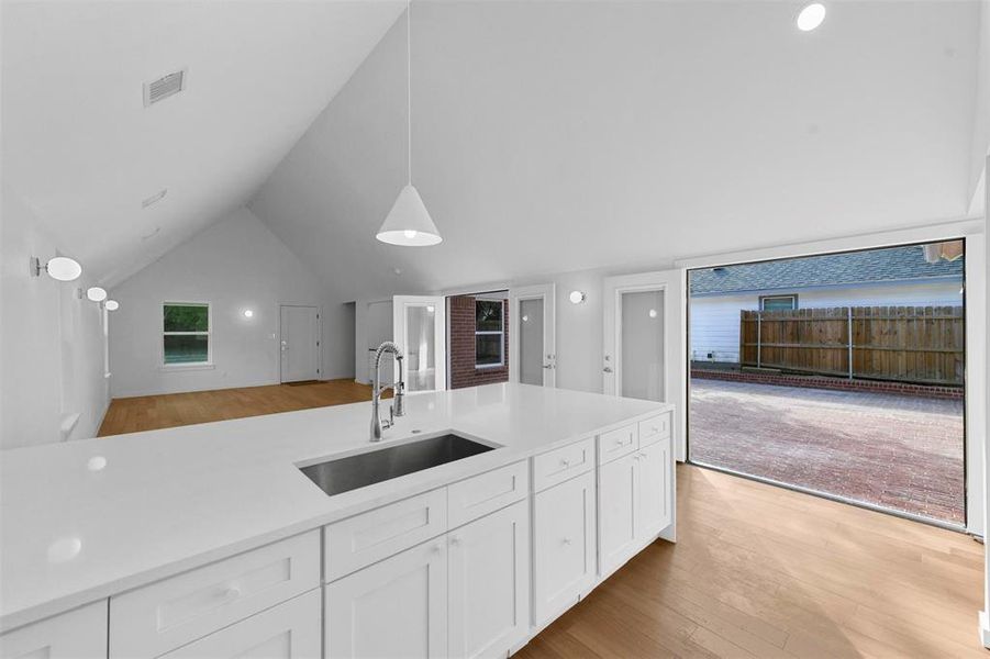 Kitchen featuring sink, light hardwood / wood-style floors, white cabinetry, vaulted ceiling, and decorative light fixtures