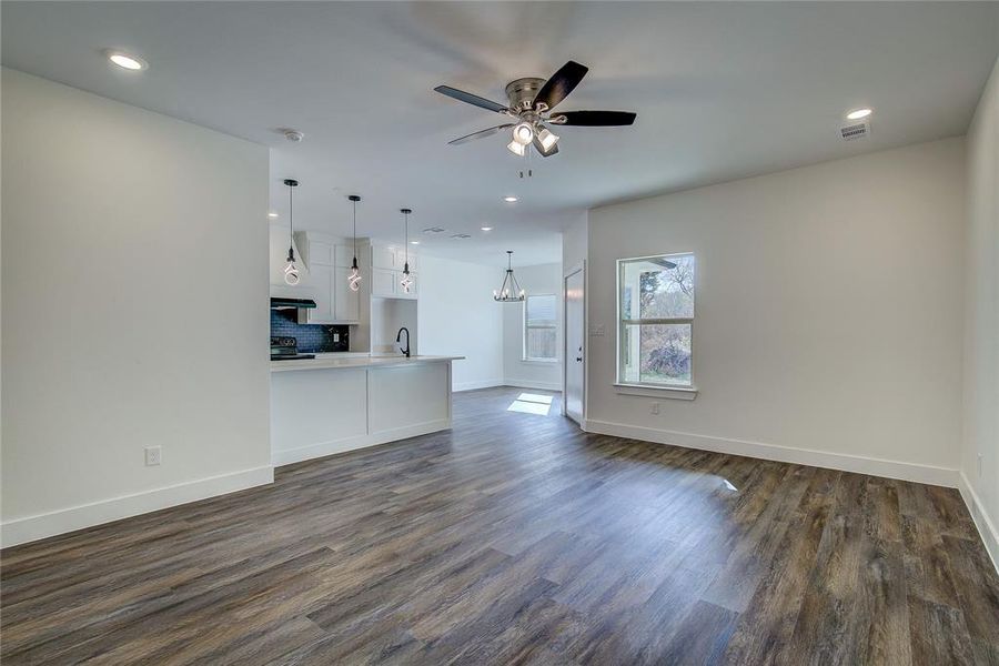 Unfurnished living room with dark wood-style flooring, recessed lighting, a ceiling fan, and a chandelier Unfurnished living room with dark wood-style flooring, recessed lighting, a ceiling fan, and a chandelier