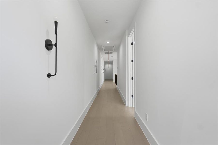 Hallway featuring light wood-finish flooring, white walls, recessed lighting, and modern black sconces