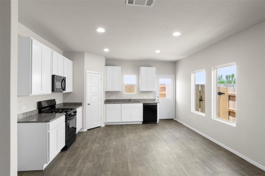 Kitchen with black appliances, recessed lighting, dark wood-style floors, white cabinetry, and dark stone counters Kitchen with black appliances, recessed lighting, dark wood-style floors, white cabinetry, and dark stone counters