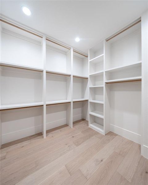 Expansive custom closet featuring light wood-finish flooring, recessed lighting, white built-in shelving, multiple hanging rods, and ample storage compartments