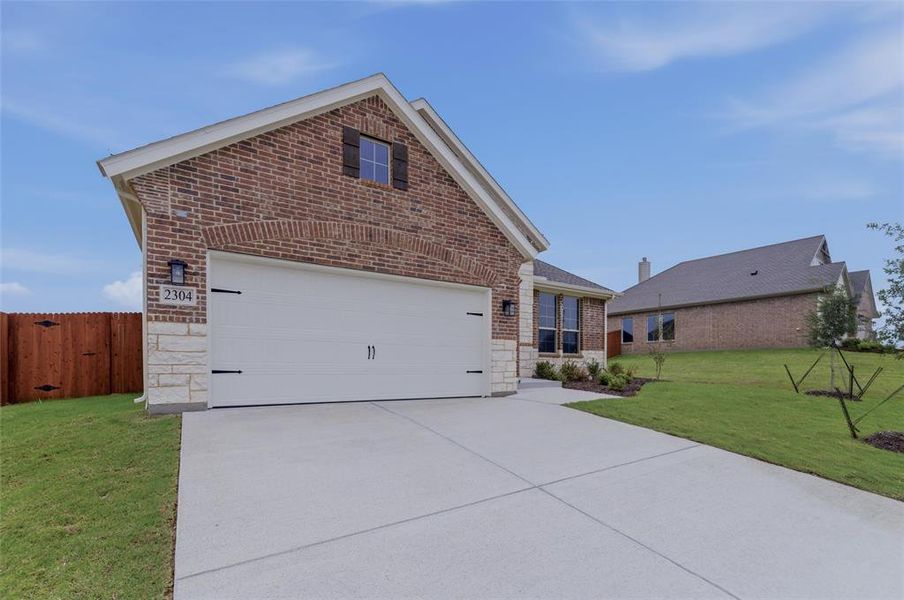 Brick and stone facade featuring a two-car garage with decorative hardware, an arched brick entryway, and a concrete driveway