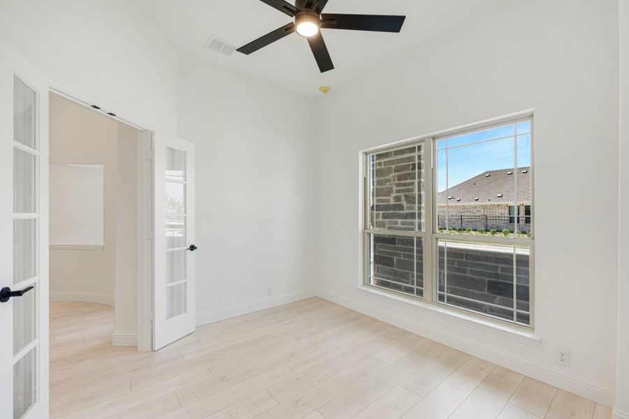 Empty room with light wood floors, ceiling fan, large window, and French doors
