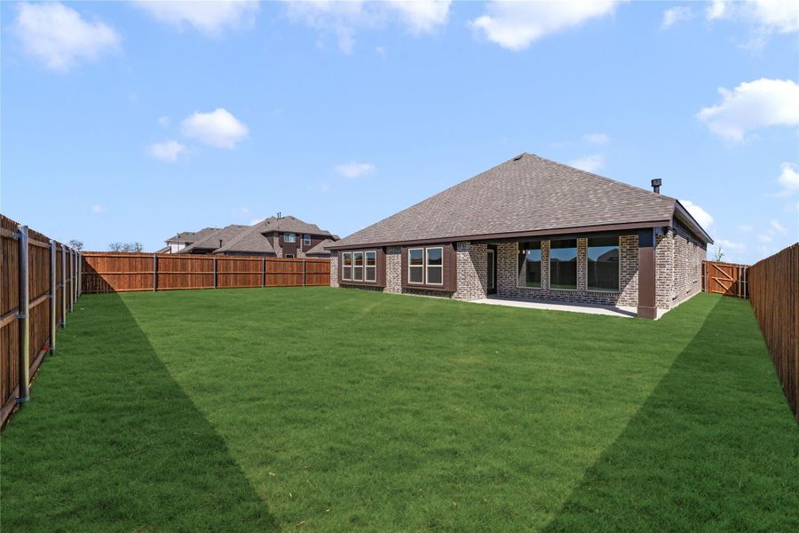 Brick home rear exterior with large fenced backyard, green lawn, and covered patio area Brick home rear exterior with large fenced backyard, green lawn, and covered patio area