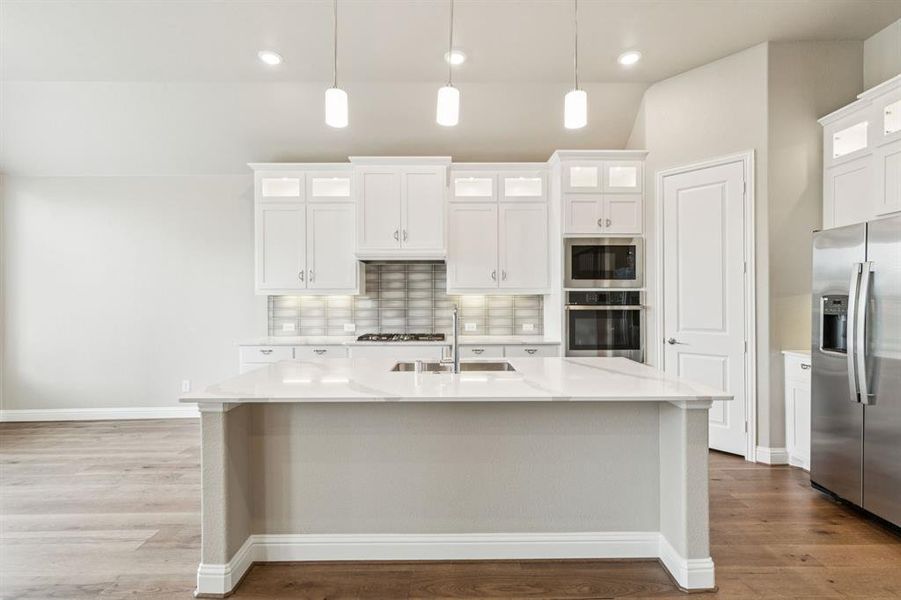 Kitchen featuring stainless steel appliances, wood finished floors, decorative backsplash, light countertops, and a kitchen island with sink