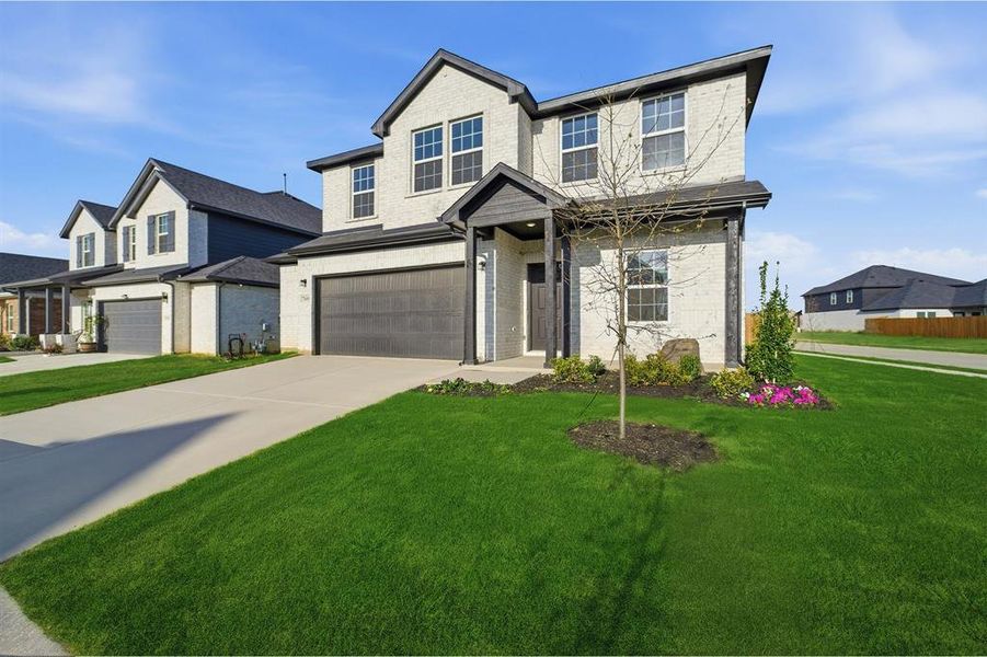 Contemporary two-story residence featuring light-colored brick exterior with dark trim accents, a two-car garage with a dark sectional door, and a covered entry