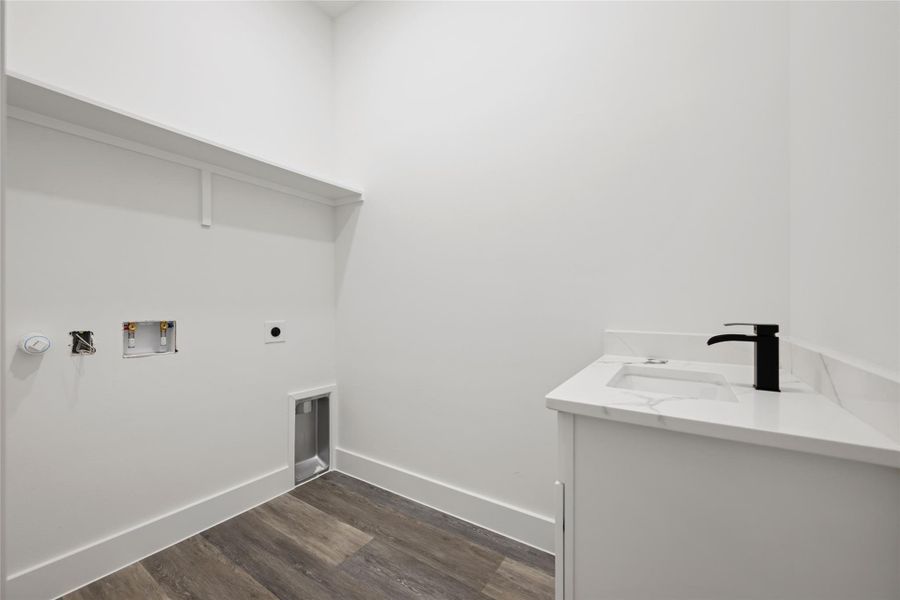 Laundry area with built-in shelving, wood-finish flooring, and a vanity featuring a white sink, matte black faucet, and stone-finish countertop