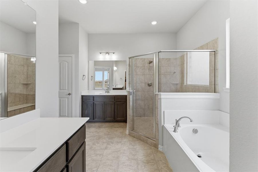 Full bath featuring two vanities, a stall shower, a bath, light tile patterned flooring, and recessed lighting