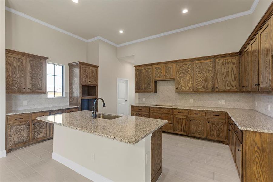 Kitchen featuring a kitchen island with sink, crown molding, sink, decorative backsplash, and light stone countertops