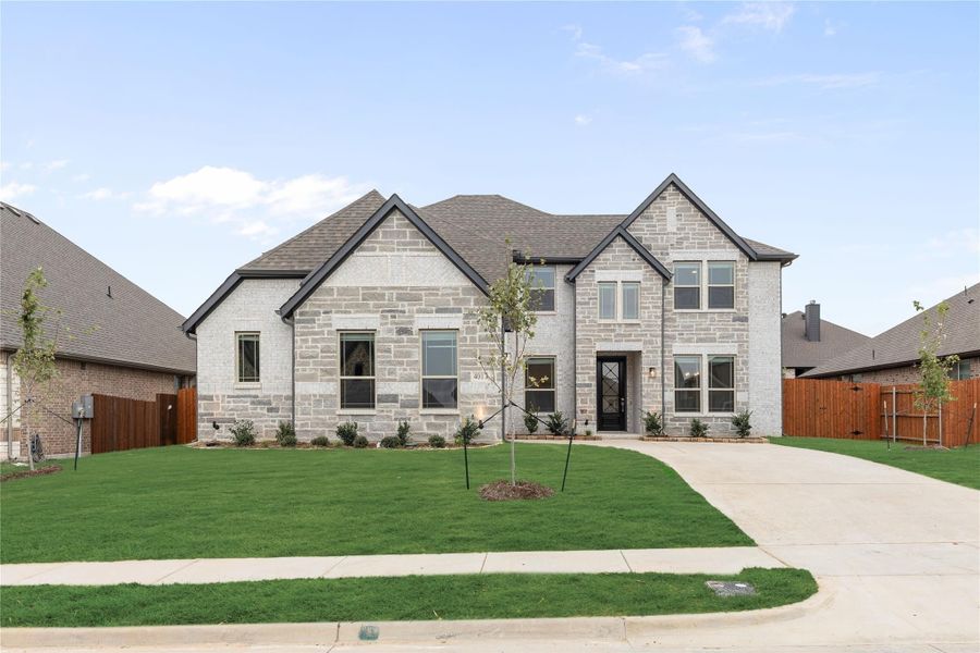 Two-story stone and brick home with dark trim, pitched roof, and manicured front lawn with concrete driveway