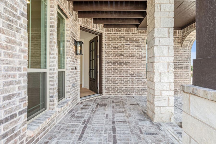 Covered front porch with brick and stone exterior, wood beam ceiling, and dark wood entry door with lantern light